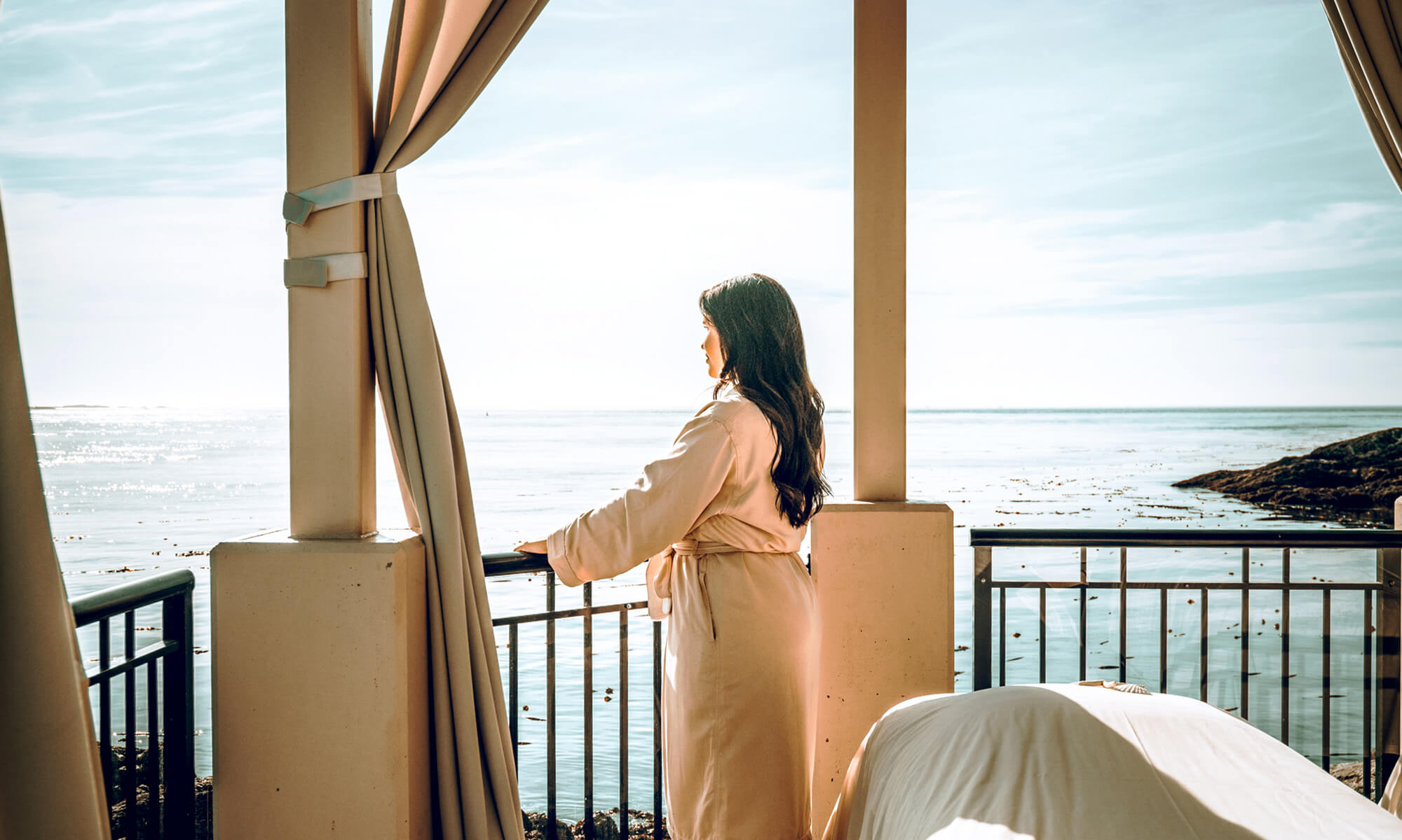 women standing on deck looking at the ocean wearing a robe large drawn curtains