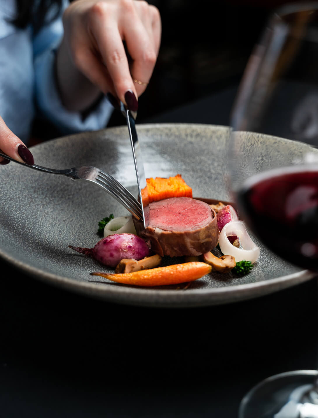 fine dining women cutting a medium rare sirloin with seasonal vegetables