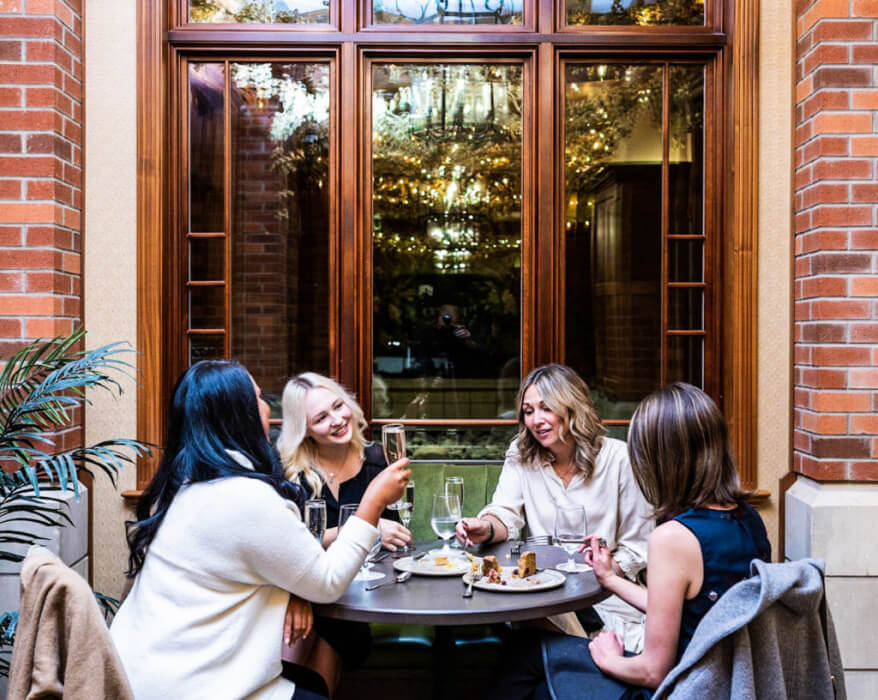 four friends sitting at a round table conversing drinking champagne and eating outdoor patio