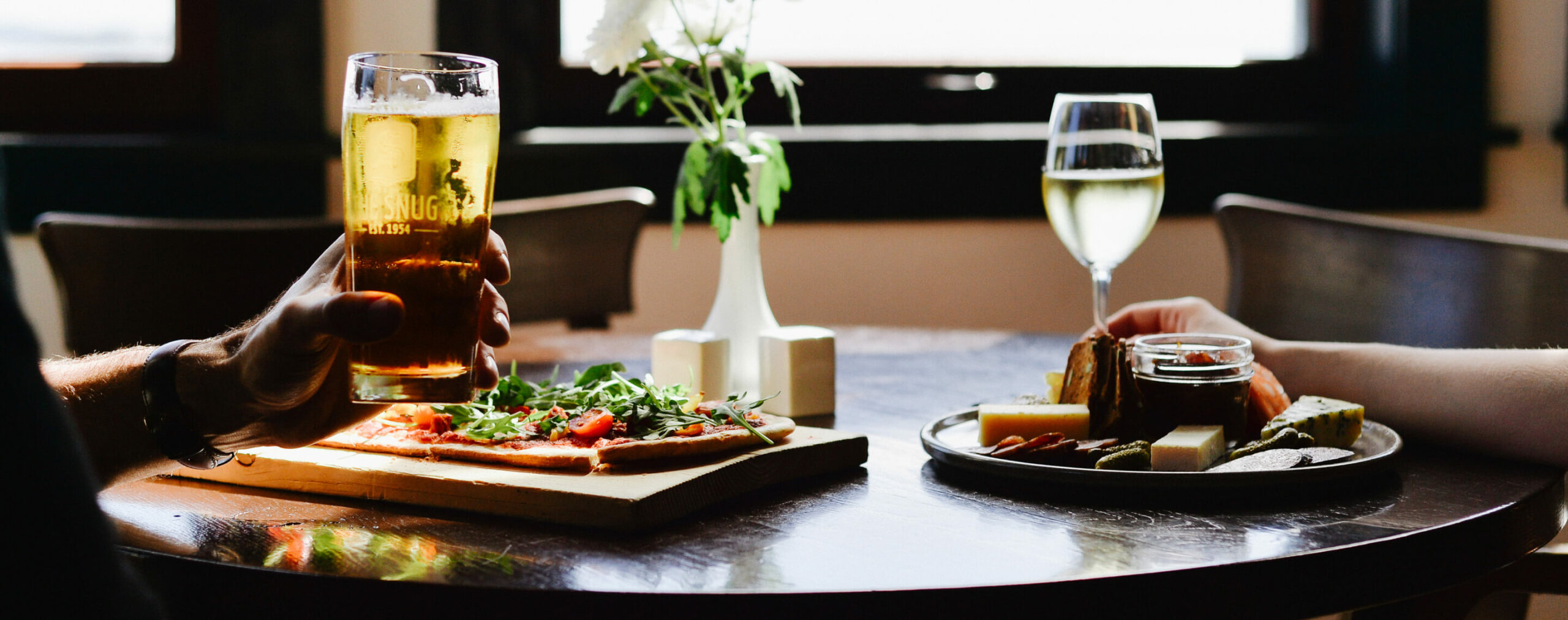 couple dining close up pizza and charcuterie plate man holding pint of beer woman holding glass white wine