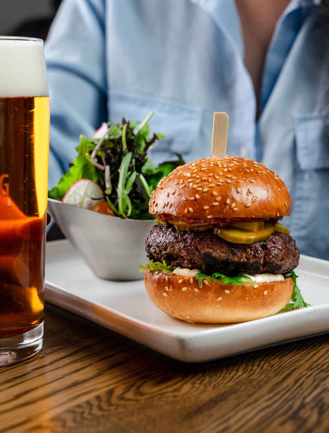 woman dining close up feature mondo burger with a fresh garden salad and pint of beer