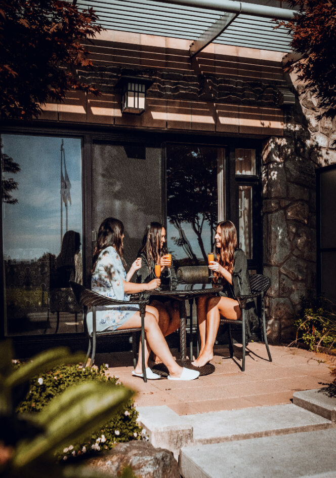 three women wearing silky robes sitting outside on patio enjoying mimosas