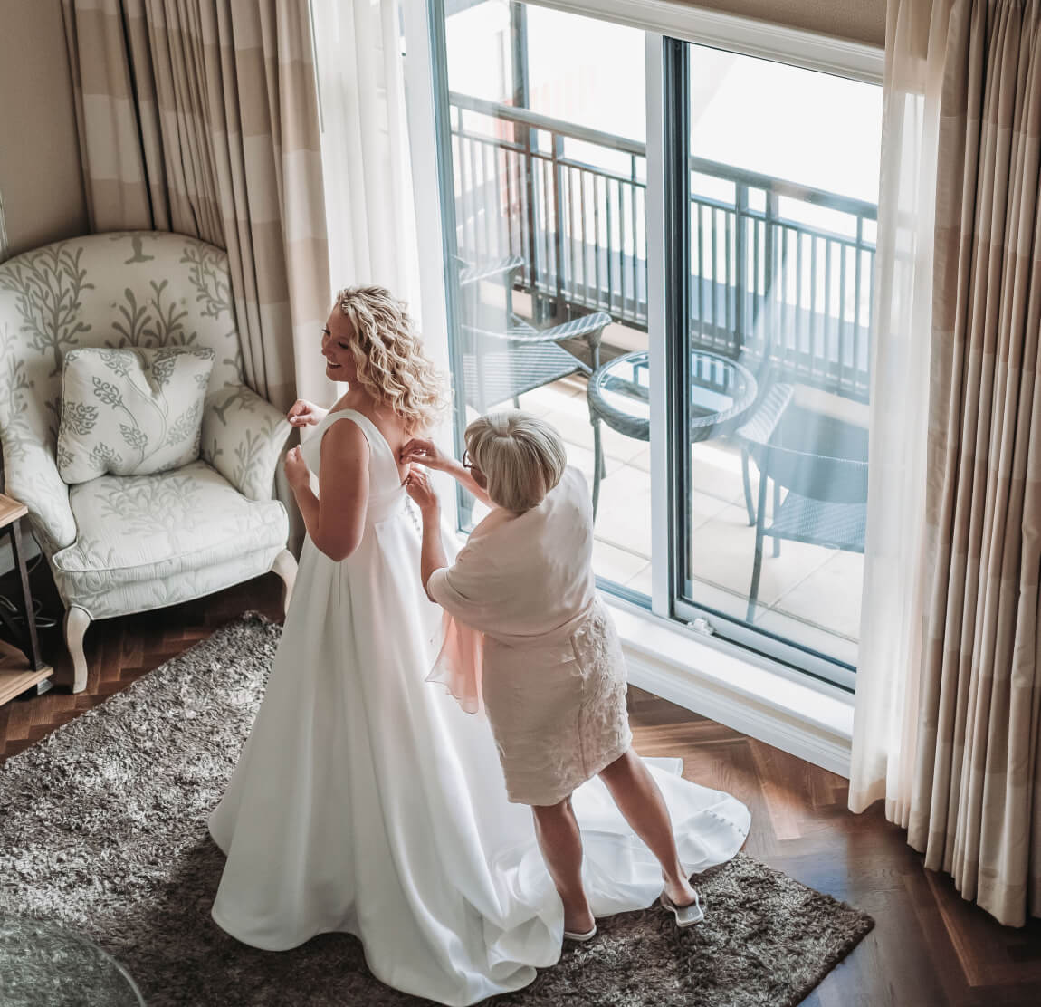 bride and mother in hotel rooming mother adjusting wedding dress clasp