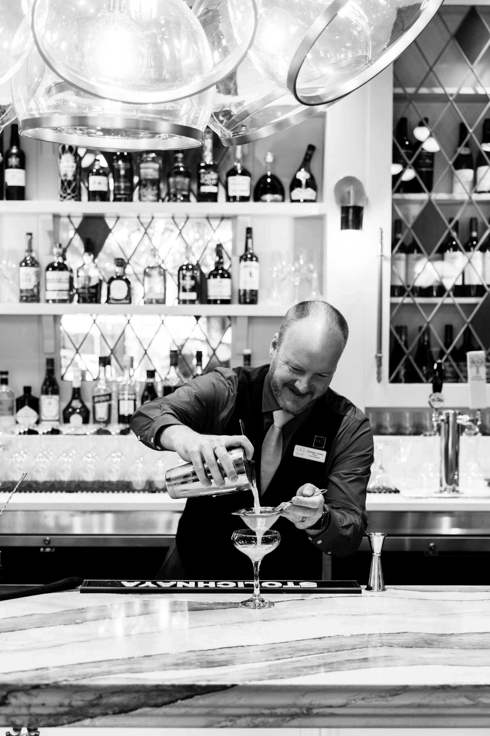 bartender at FARO pizza bar pouring a cocktail with a variety of liqueurs and wine bottles behind him