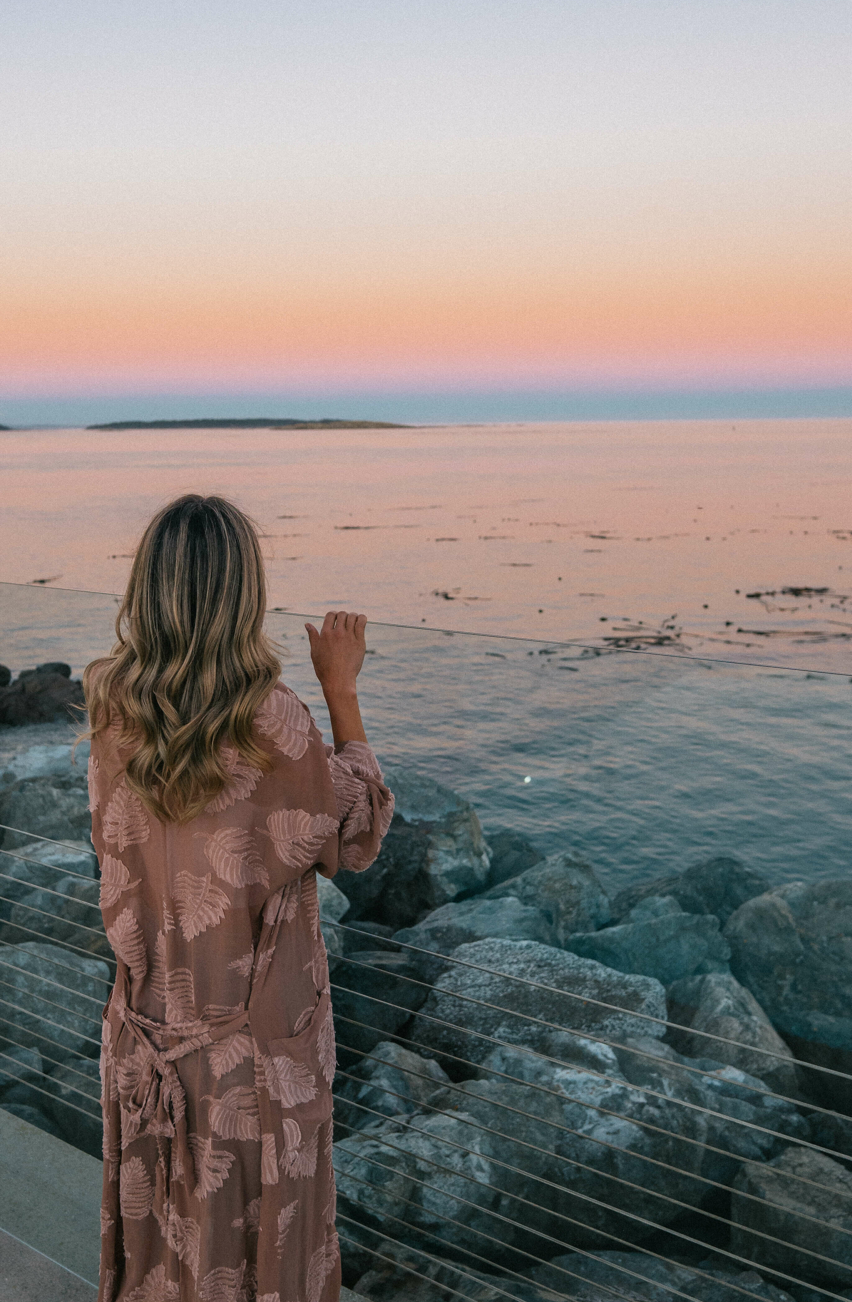 beautiful woman in pink robe looking into the distance at sunset over pacific ocean