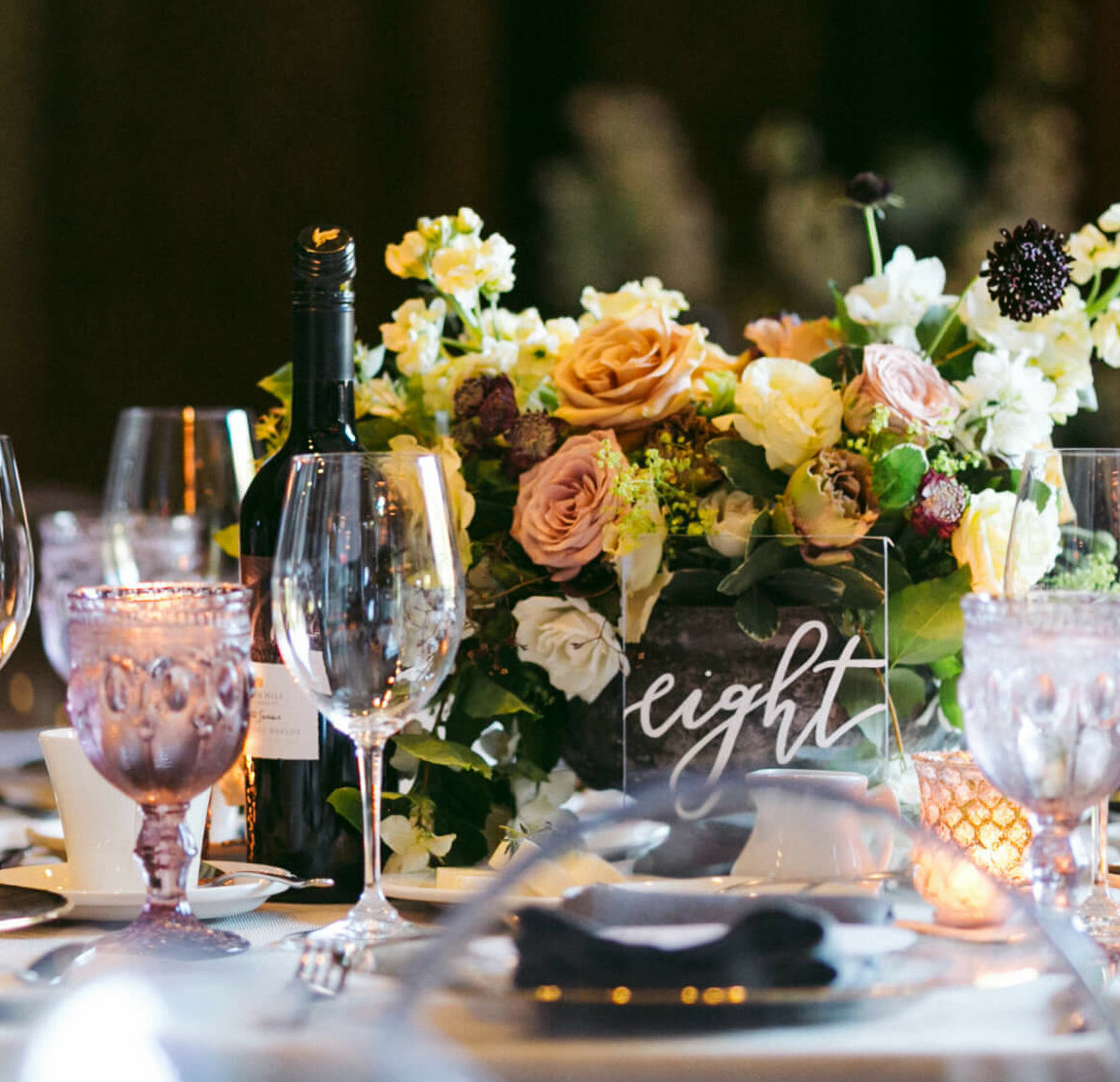 a wedding table decorated with spring florals, table number and purple wine glasses