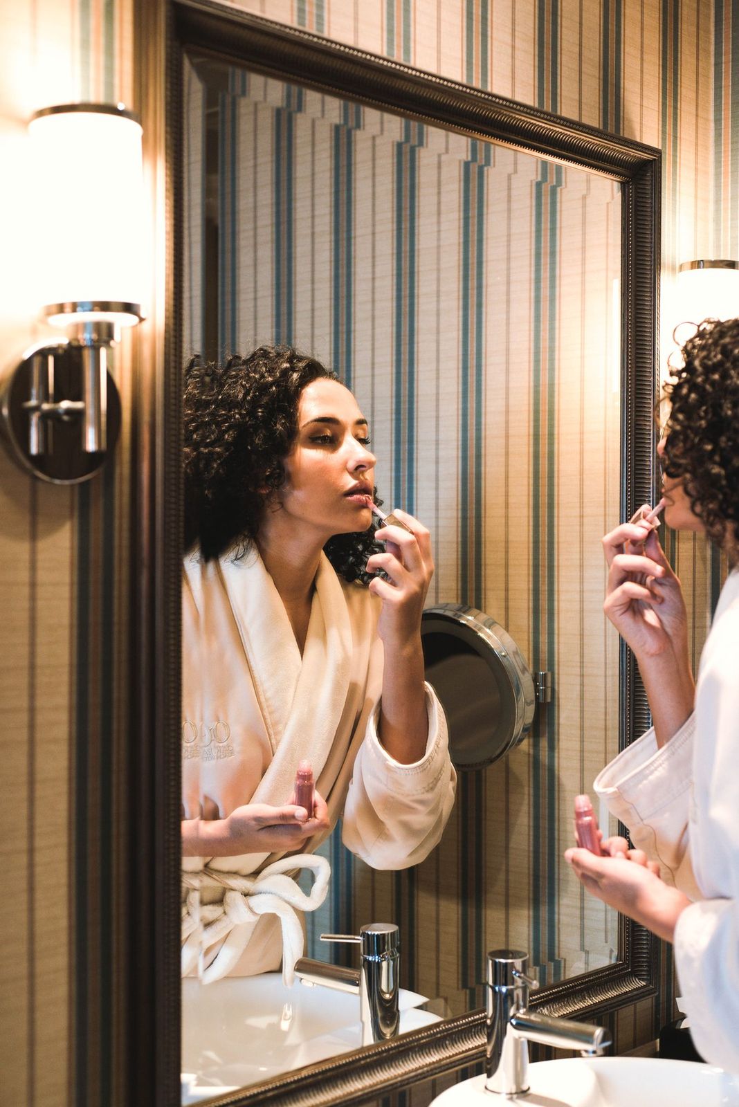 woman applying lipstick looking in bathroom mirror