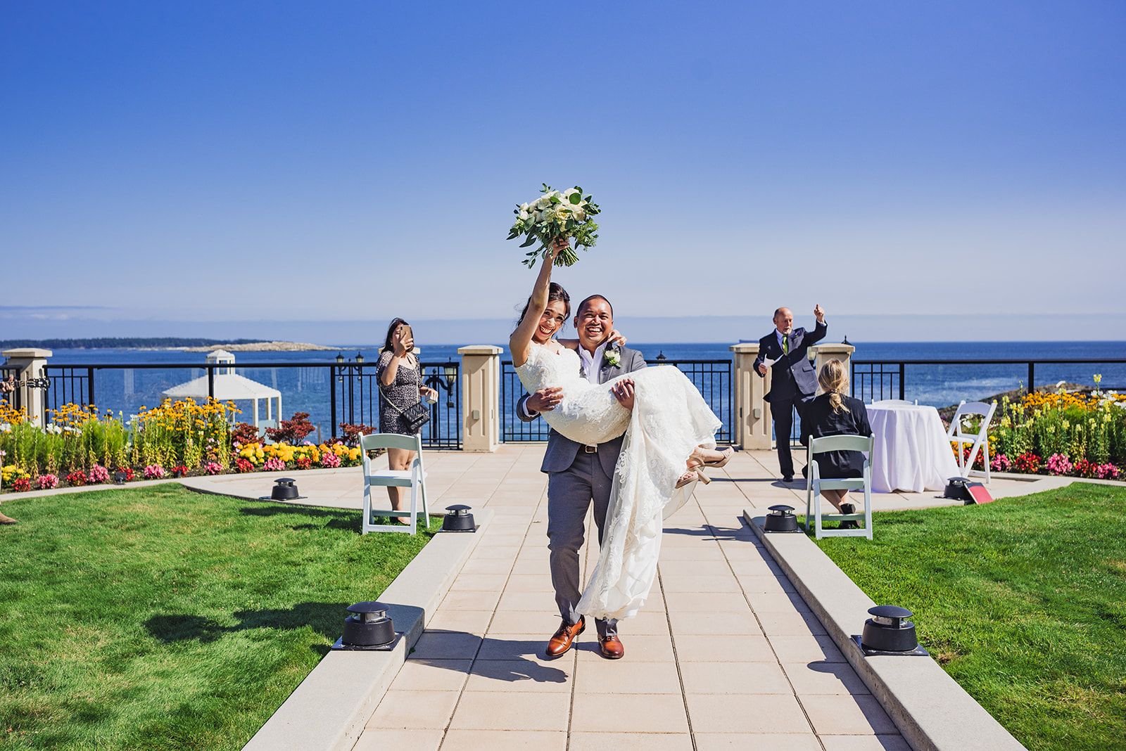 groom carrying bride down walkway outside wedding