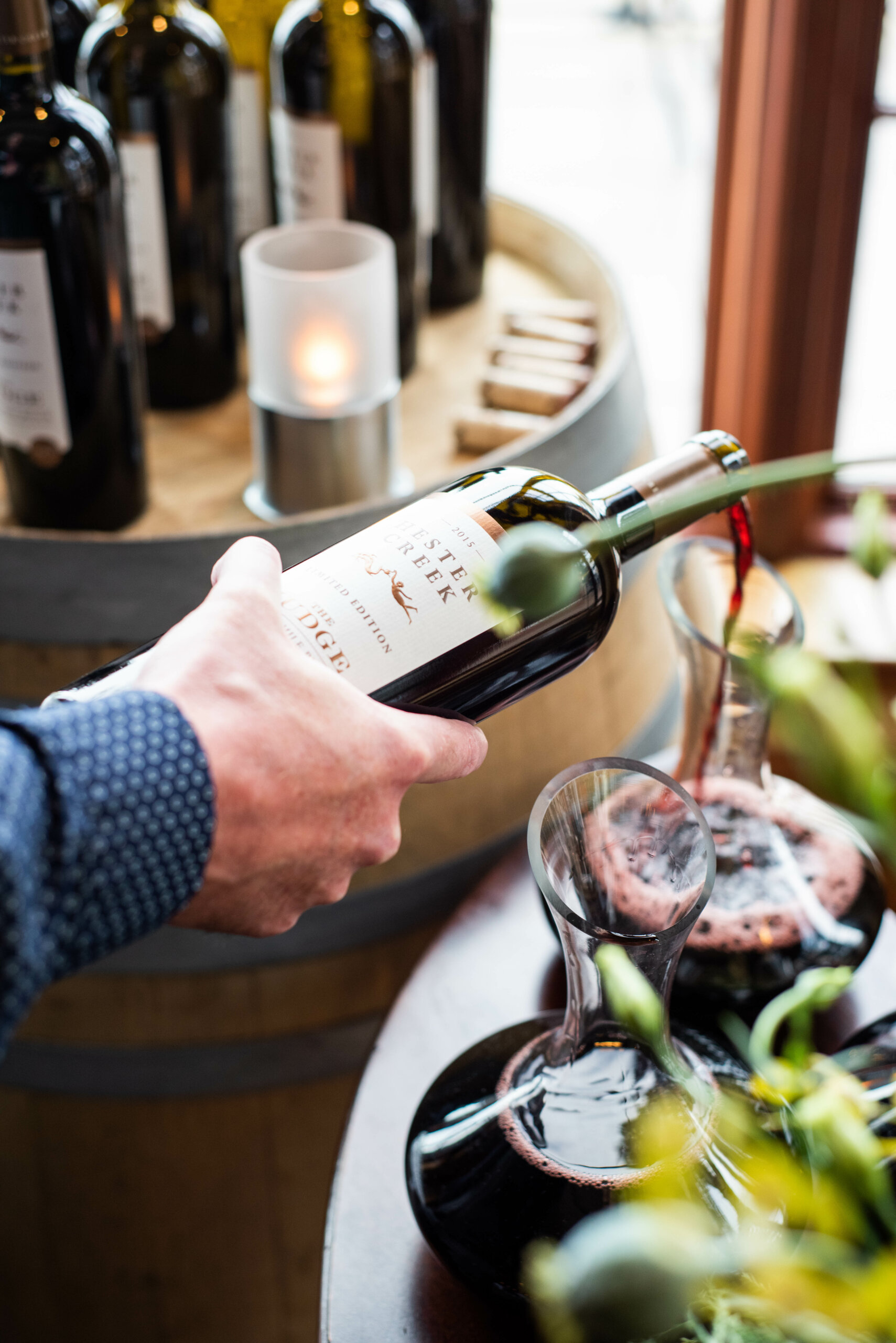 Hester Creek's The Judge red wine being poured into a decanter with candles and wine bottles in the background