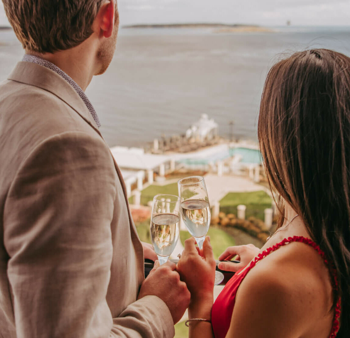 couple cheering sparkling wine with ocean view backdrop in distance